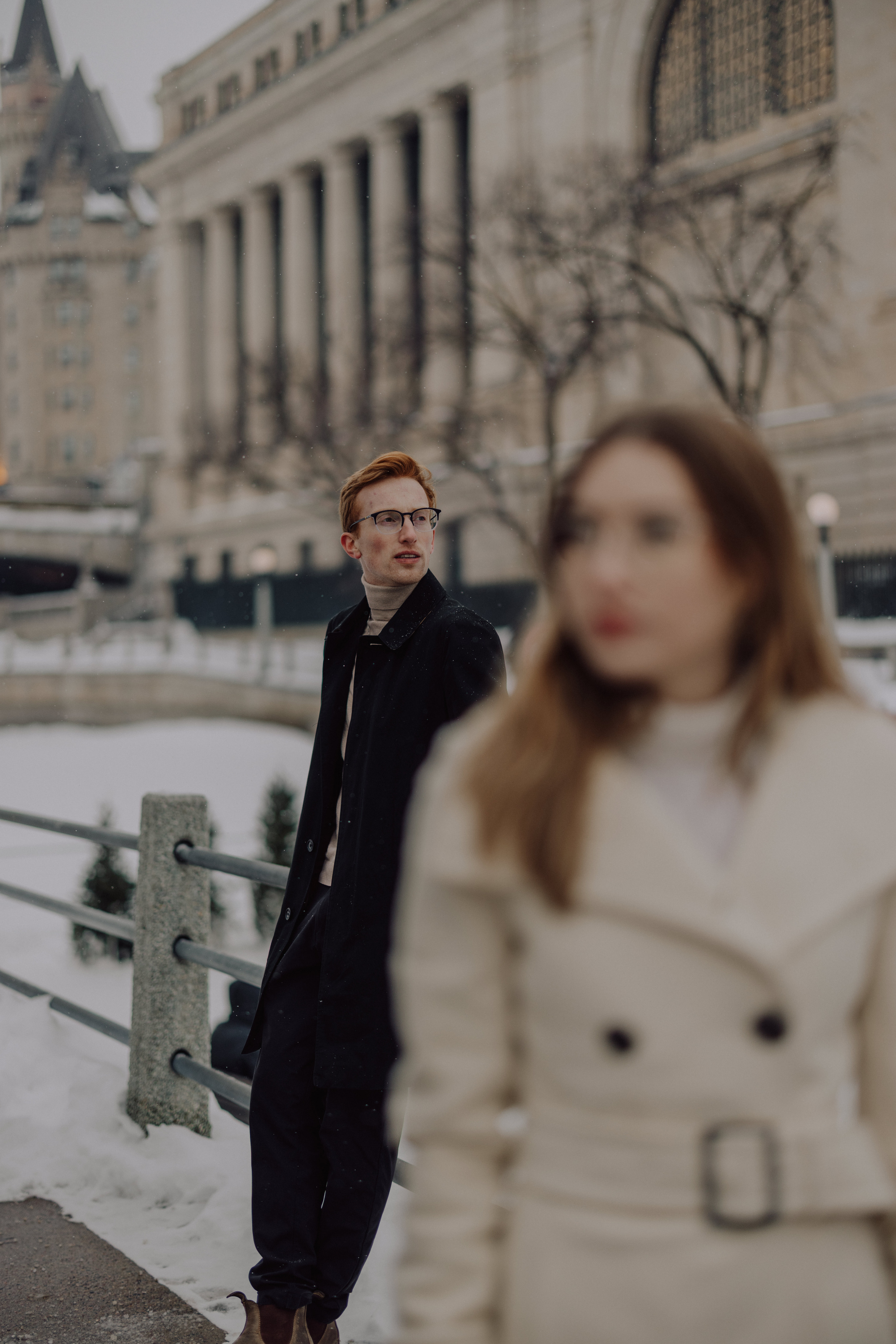 Alex in a black coat in downtown Ottawa, with Parliament in the distance